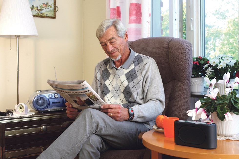 Man med trygghetslarm sitter och läser en tidning